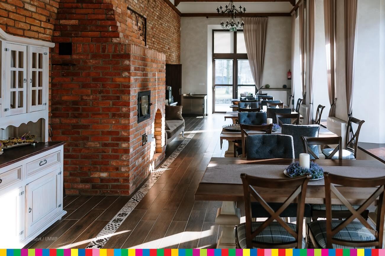 Wnętrze Gacówki z ceglanym piecem i restauracyjnymi stolikami.