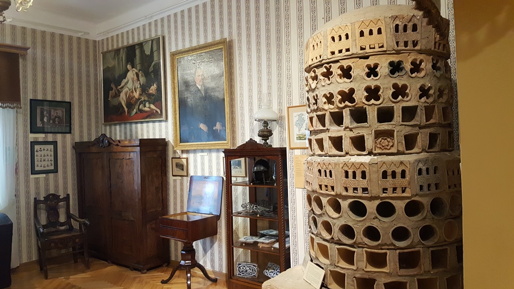 Wnętrze domu talmudycznego, w rogu stoi piec, gabloty i kredens