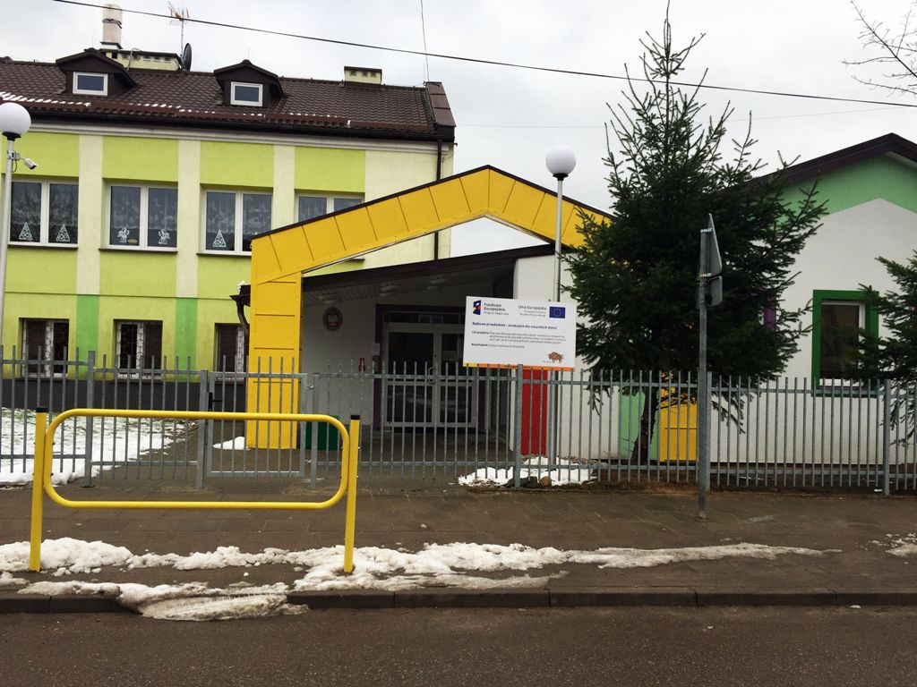 Wejście do przedszkola, widok na starszą i dobudowaną część przedszkola. Przed wejściem tablica informacyjna 