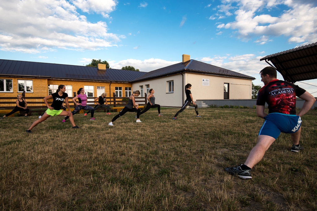 Uczestnicy zajęć fitness ćwiczą przed budynkiem centrum. 