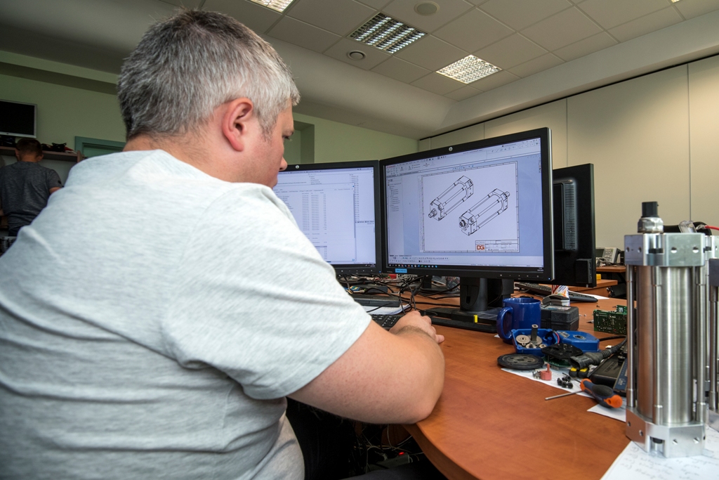 Mężczyzna pracuje nad projektami przy komputerze. Elementy systemu leżą obok na biurku. 
